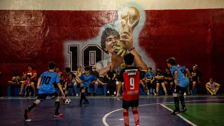 BUENOS AIRES, ARGENTINA - OCTOBER 30: Kids play football in front of a mural of Diego Armando Maradona holding the world cup at Juventud Unida de Barracas Club on October 30, 2021 in Buenos Aires, Argentina. Football fans all over the country remember their late idol, who would have turned 61 on October 30. (Photo by Tomas Cuesta/Getty Images)