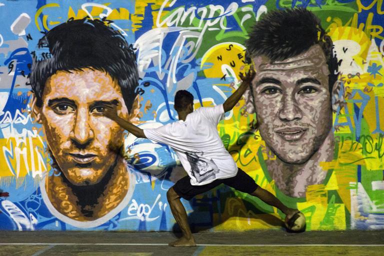 Youngsters play football in front of a mural of Argentine football player Lionel Messi (L) and Brazil's player Neymar da Silva Santos Junior at a field of Tavares Bastos shantytown (favela) in Rio de Janeiro, Brazil on June 8, 2014, just four days ahead of the FIFA World Cup 2014.  AFP PHOTO / YASUYOSHI CHIBA        (Photo credit should read YASUYOSHI CHIBA/AFP via Getty Images)